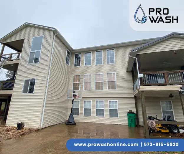 Three-story beige vinyl-sided house with many windows and covered decks, driveway with portable basketball hoop and green trash bin; ProWash logo and web overlay.